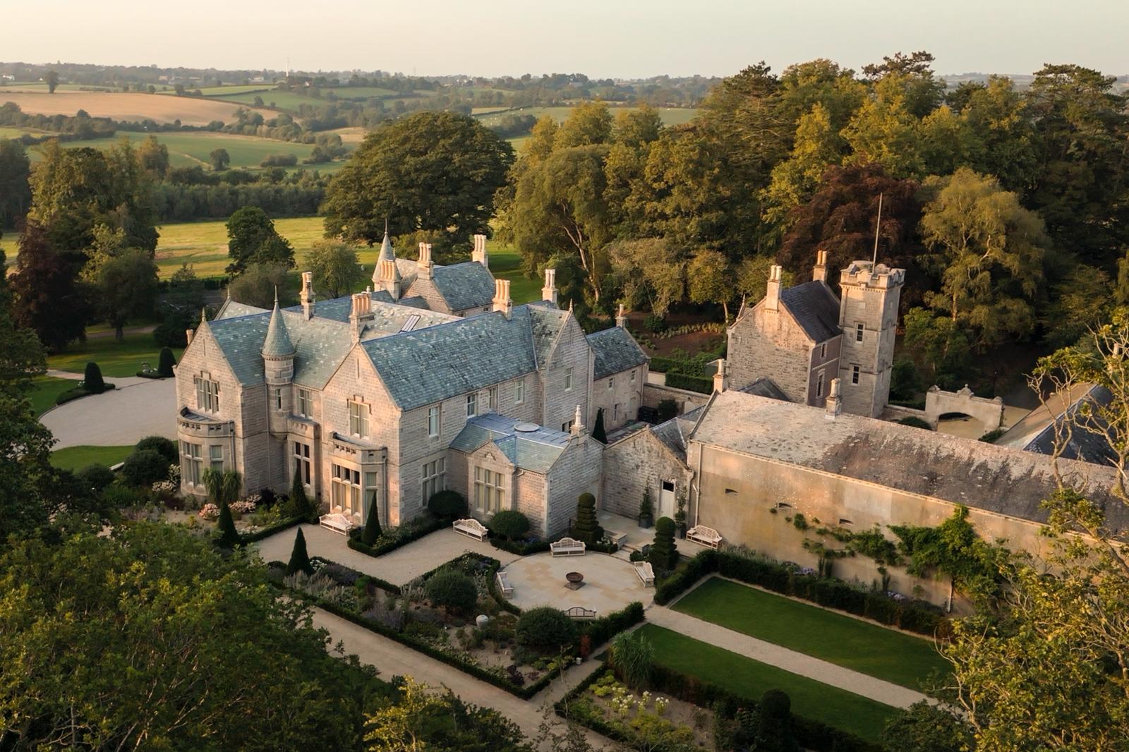 Aerial view of Gilford Castle Estate surrounded by formal gardens, woodland and rolling countryside at golden hour.